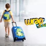 Niño de espaldas caminando en aeropuerto con maleta infantil con ruedas tipo rolling suitcase y mochila de dinosaurio