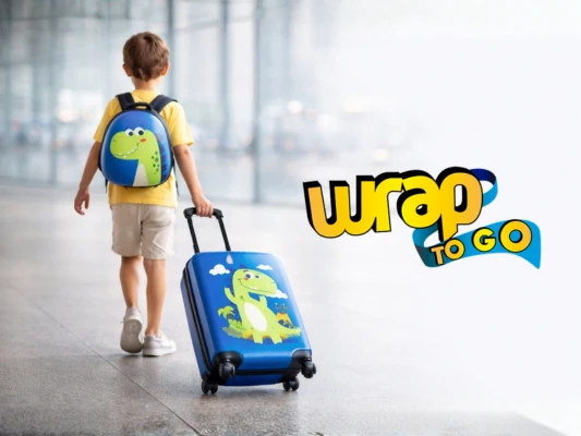 Niño de espaldas caminando en aeropuerto con maleta infantil con ruedas tipo rolling suitcase y mochila de dinosaurio