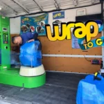 Operario realizando embalaje de maletas a domicilio con film azul sobre una maleta de viaje con ruedas en una unidad móvil.